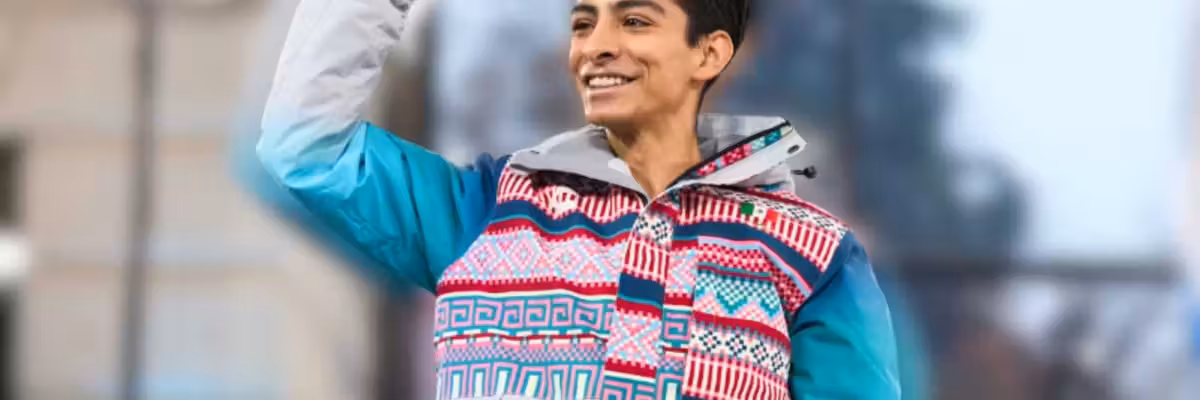 Smiling person in colorful jacket raising their fist triumphantly outdoors.