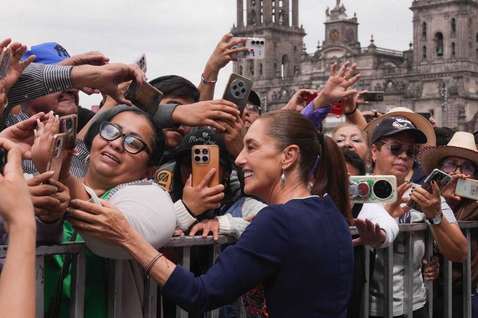 Smiling woman greets excited crowd taking photos near a historic building.