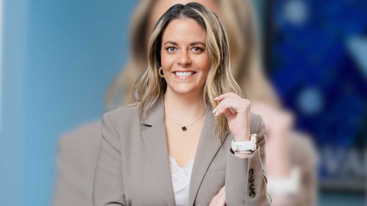 Smiling woman in a beige blazer against a blurred blue background.