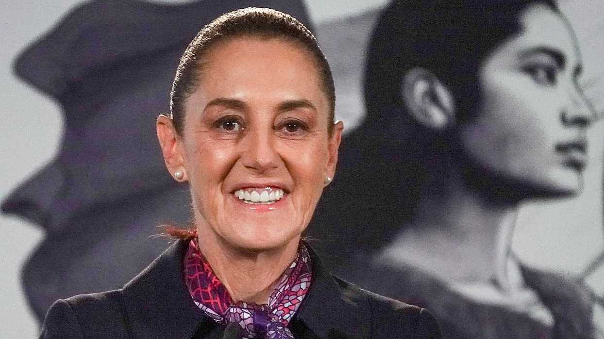 Smiling woman in a dark blazer and patterned scarf, with a black-and-white portrait behind her.