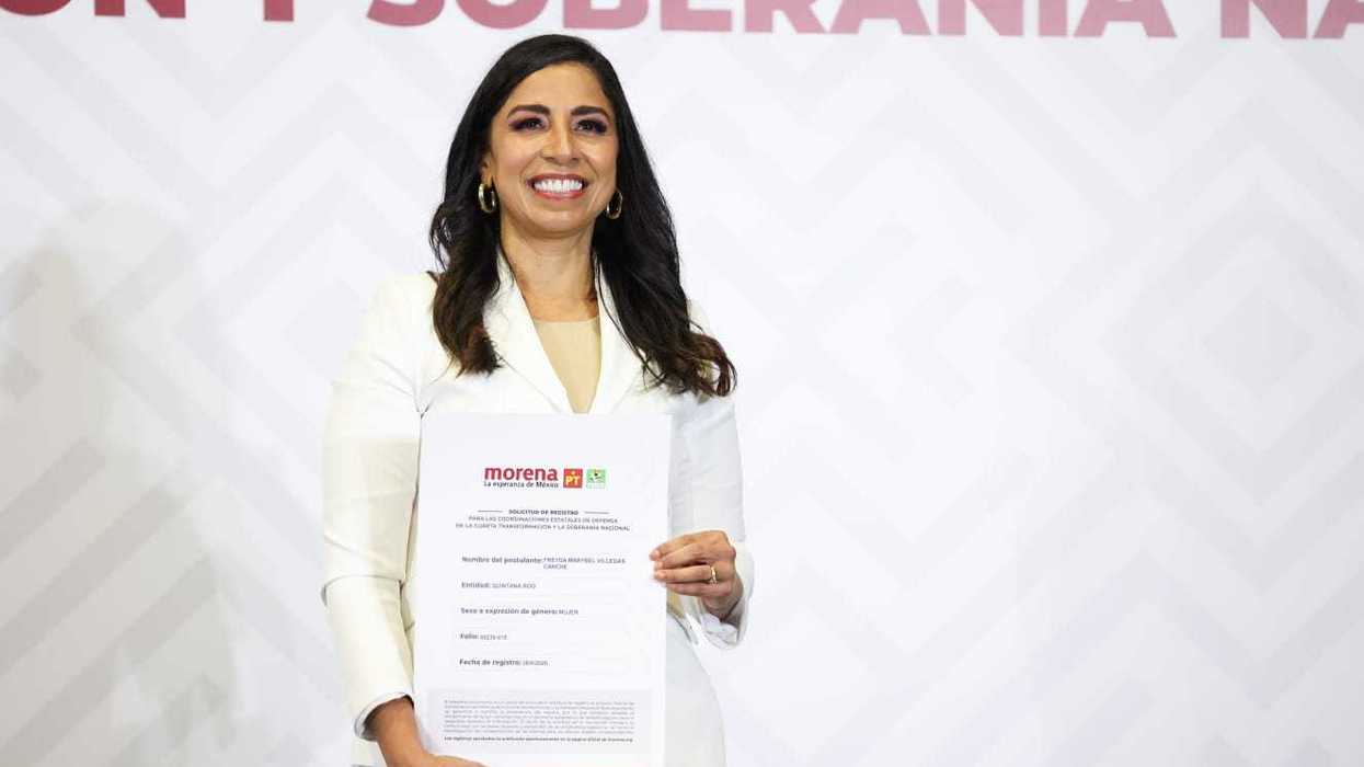 Smiling woman in white suit holds document against a patterned background.