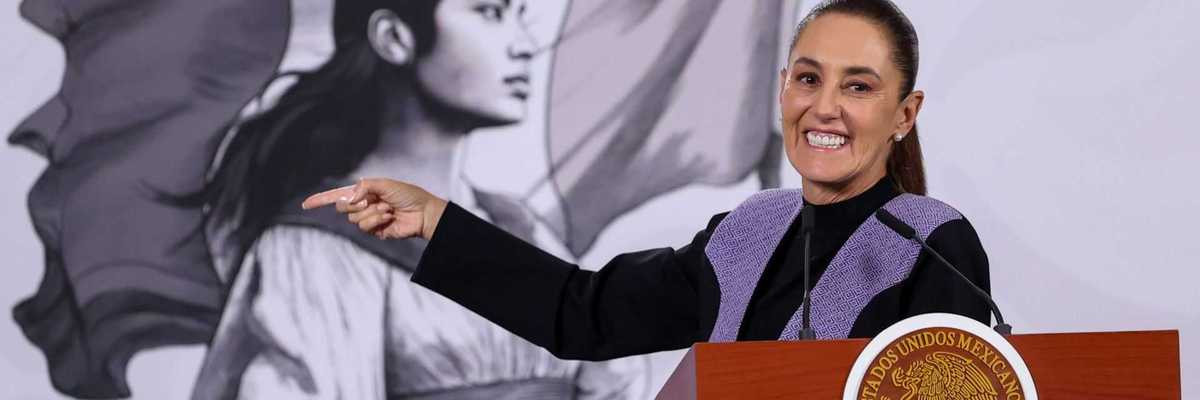 Smiling woman pointing at podium, mural of woman with flag in background.