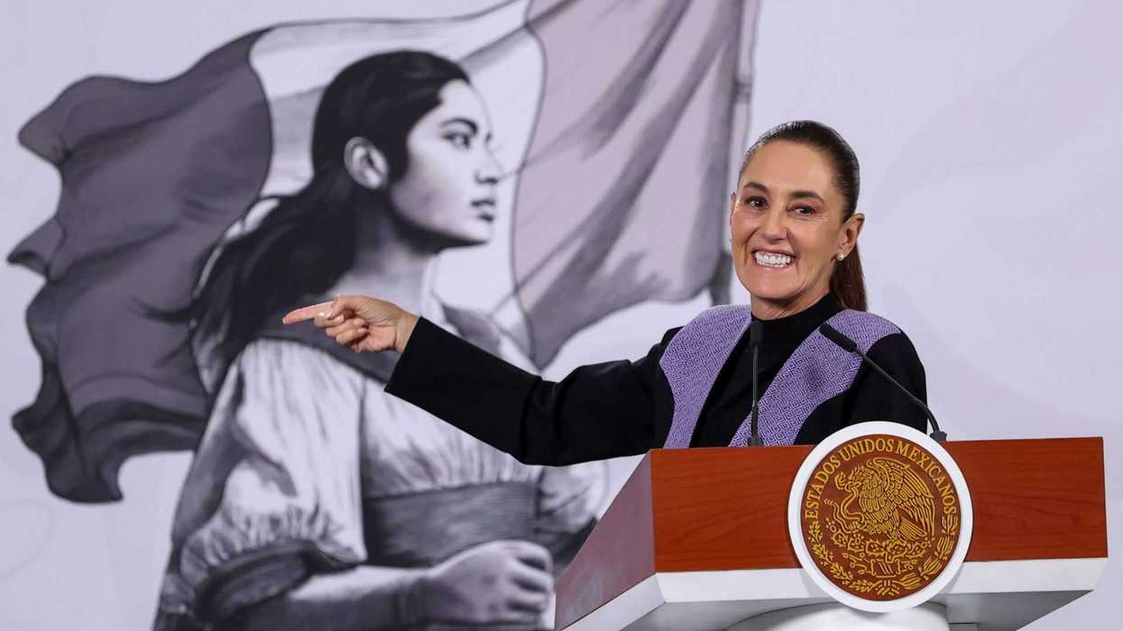 Smiling woman pointing at podium, mural of woman with flag in background.