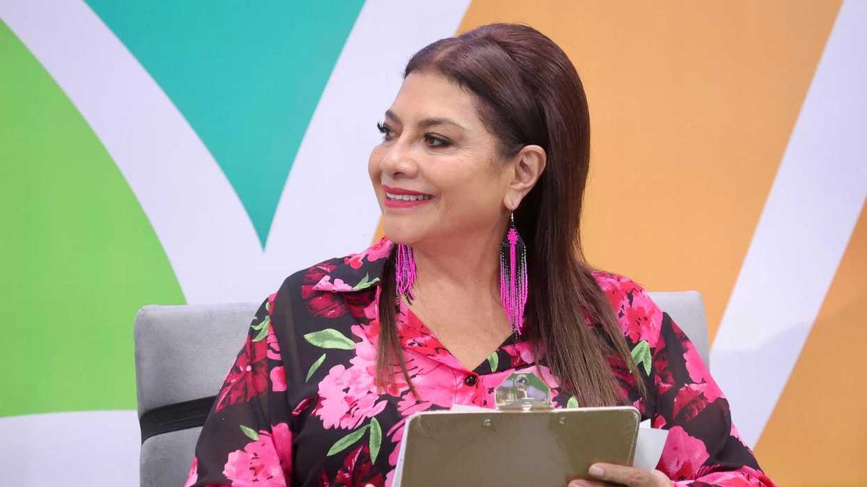 Smiling woman with clipboard in floral outfit and pink earrings, on colorful background.