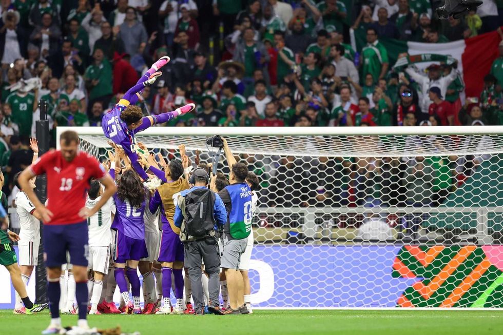 Soccer fans celebrate by lifting a player near the goal, with spectators in the background.