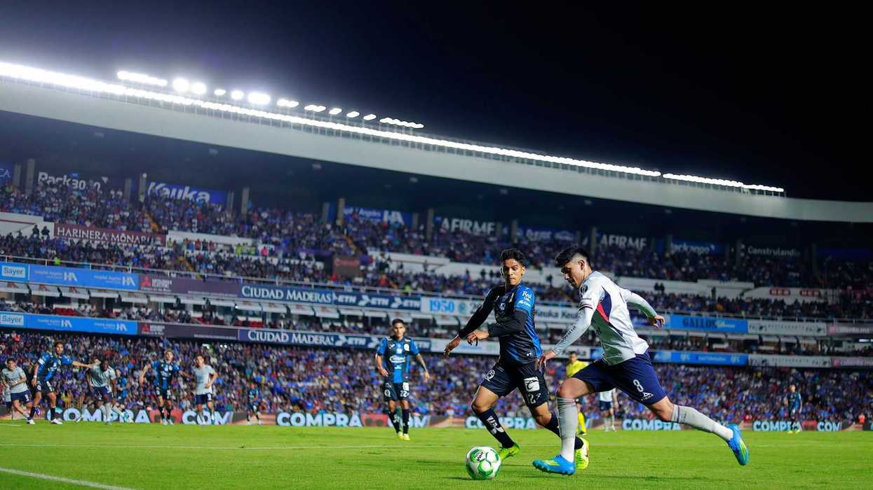 Soccer match at a crowded stadium under bright lights, players competing for the ball.