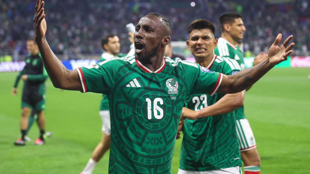 Soccer player celebrating enthusiastically in a green jersey with teammates in the background.