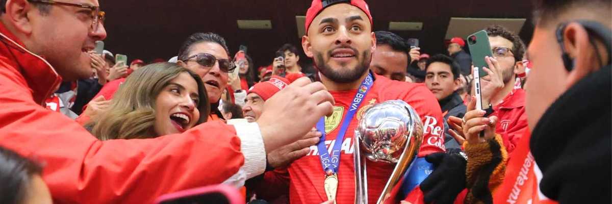 Soccer player holding a trophy, surrounded by excited fans taking photos.