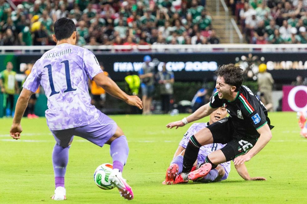Soccer player in black jersey falls to the ground during intense match on a green field.