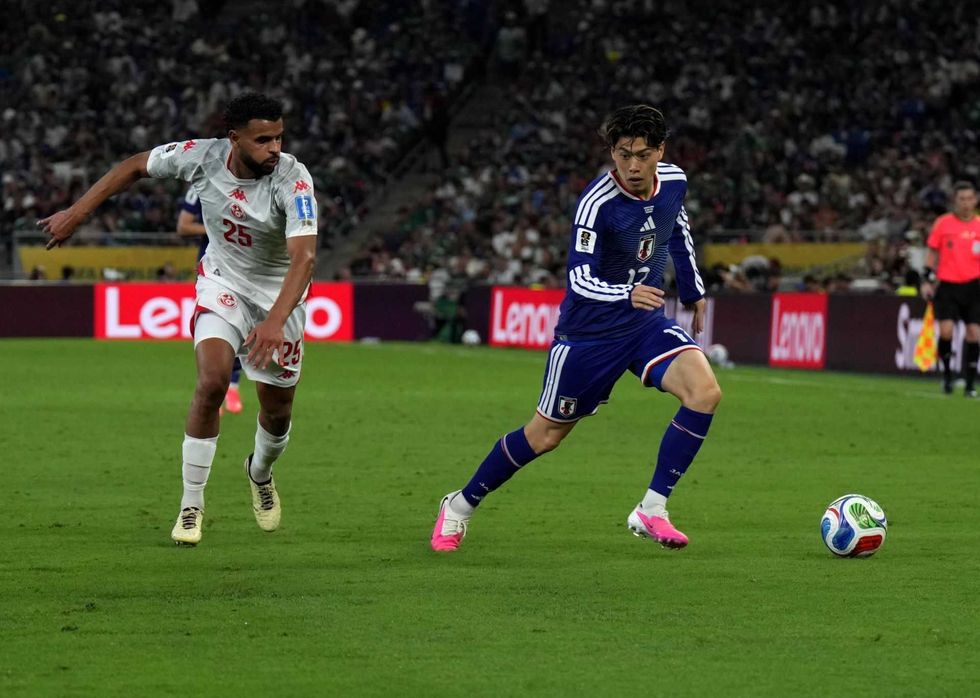 Soccer player in blue controls ball while opponent in white chases on the field.