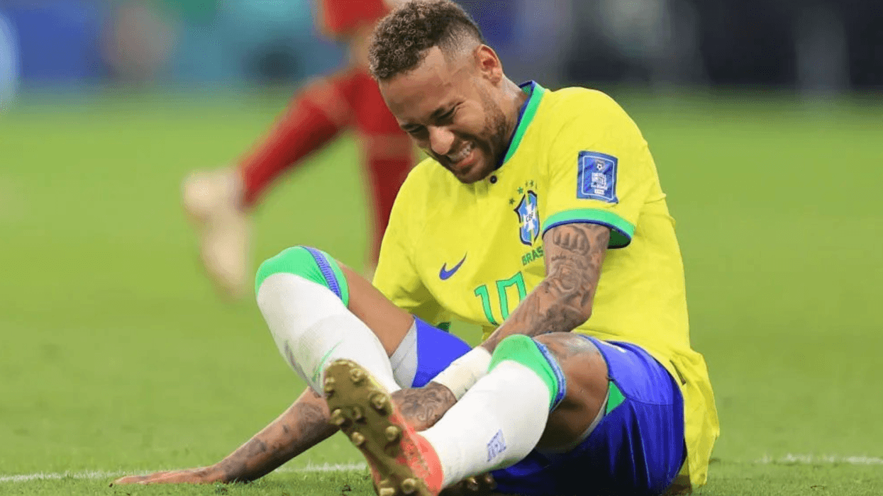 Soccer player in yellow jersey sitting on field, appearing injured and in pain.