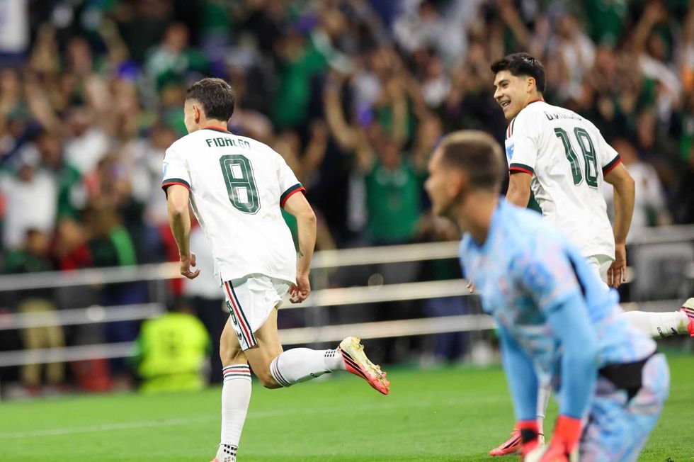 Soccer players celebrate a goal on the field as the crowd cheers in the background.