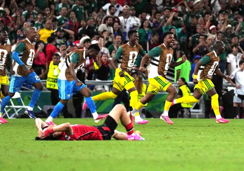 Soccer players celebrate as one opponent lies on the field, crowd cheering behind.