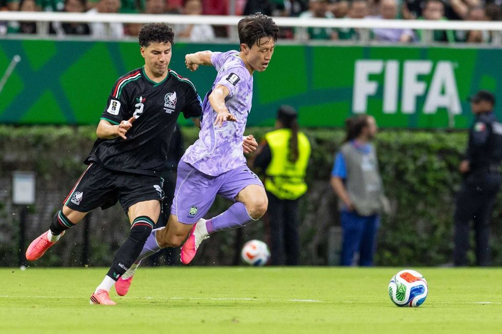 Soccer players in action during a FIFA match, with one player running and another defending.