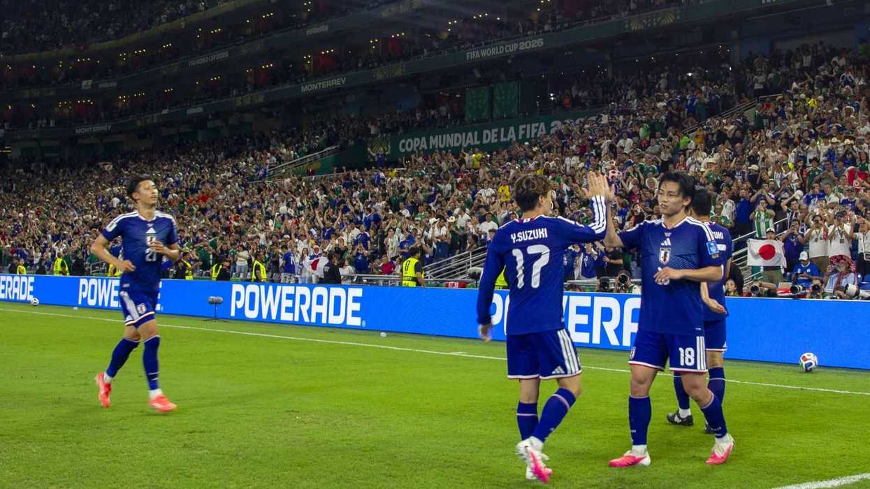 Soccer players in blue celebrate a goal in a packed stadium during a FIFA tournament.