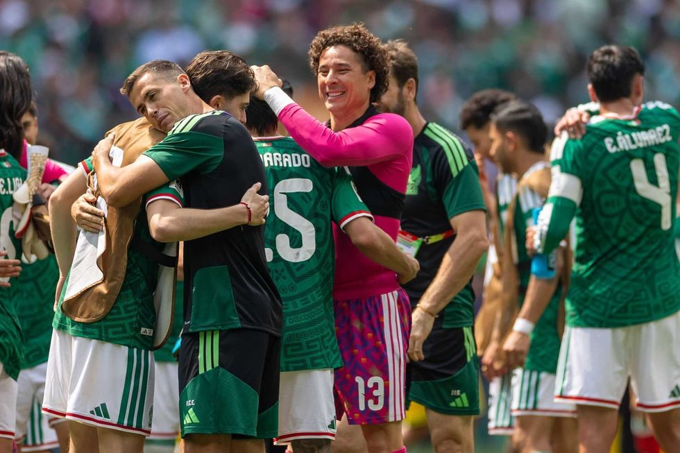 Soccer players in green and pink jerseys hug and celebrate on the field.