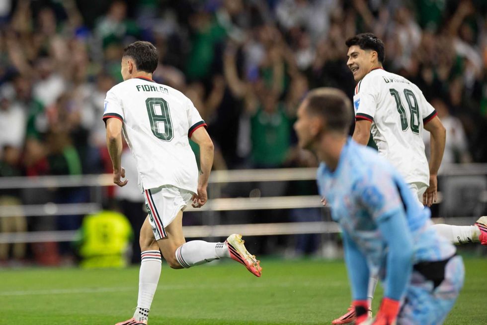 Soccer players in white uniforms celebrate a goal on the field.