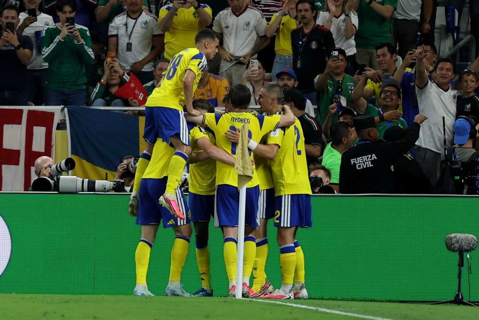 Soccer players in yellow celebrate a goal, surrounded by cheering fans and photographers.