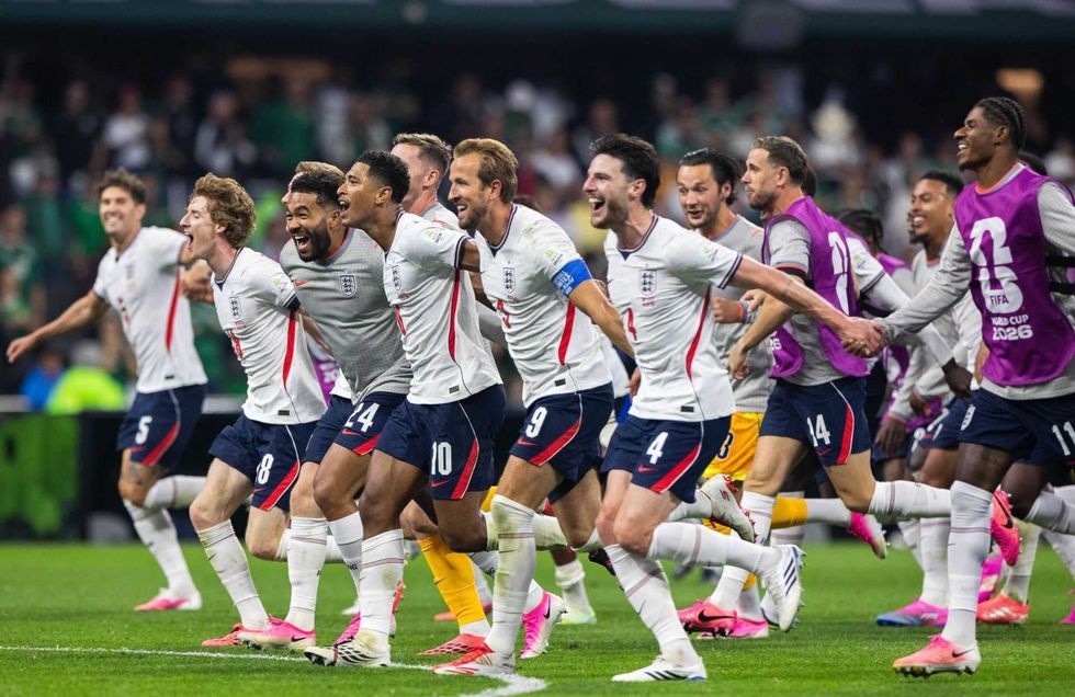 Soccer team celebrates, running across the field, wearing white and navy uniforms with flags.