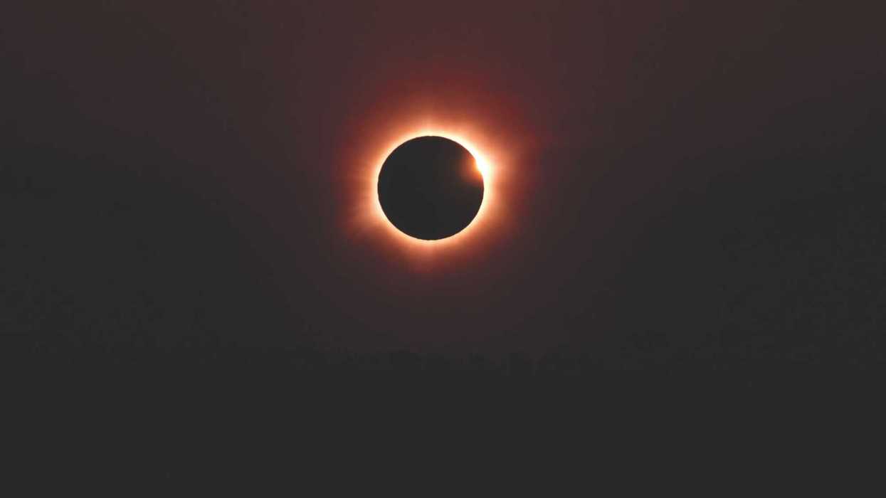 Solar eclipse with a glowing red-orange ring against a dark sky.