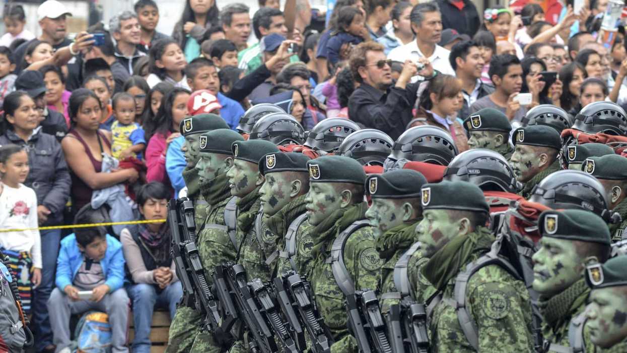 Soldiers in camouflage march past a crowd of spectators taking photos.