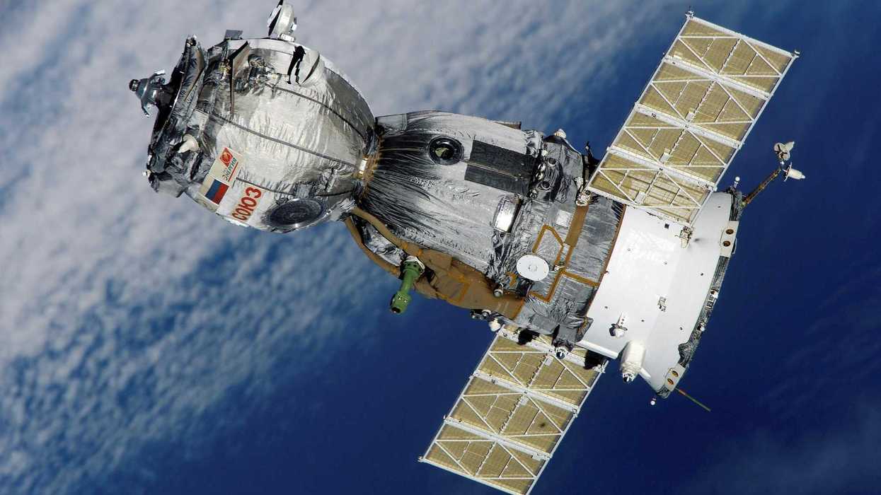 Spacecraft with solar panels orbiting above Earth’s clouds.