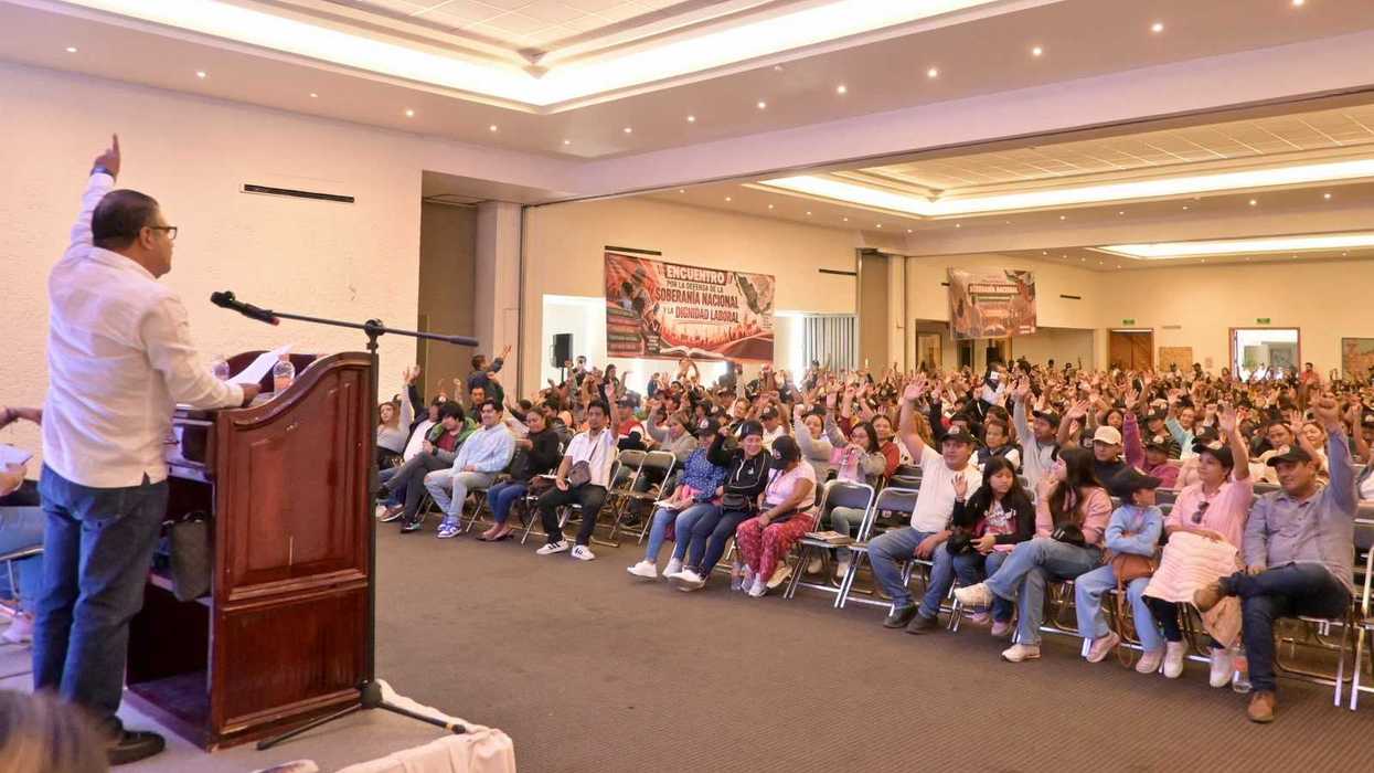 Speaker addresses a large audience in a conference hall, attendees raising hands.