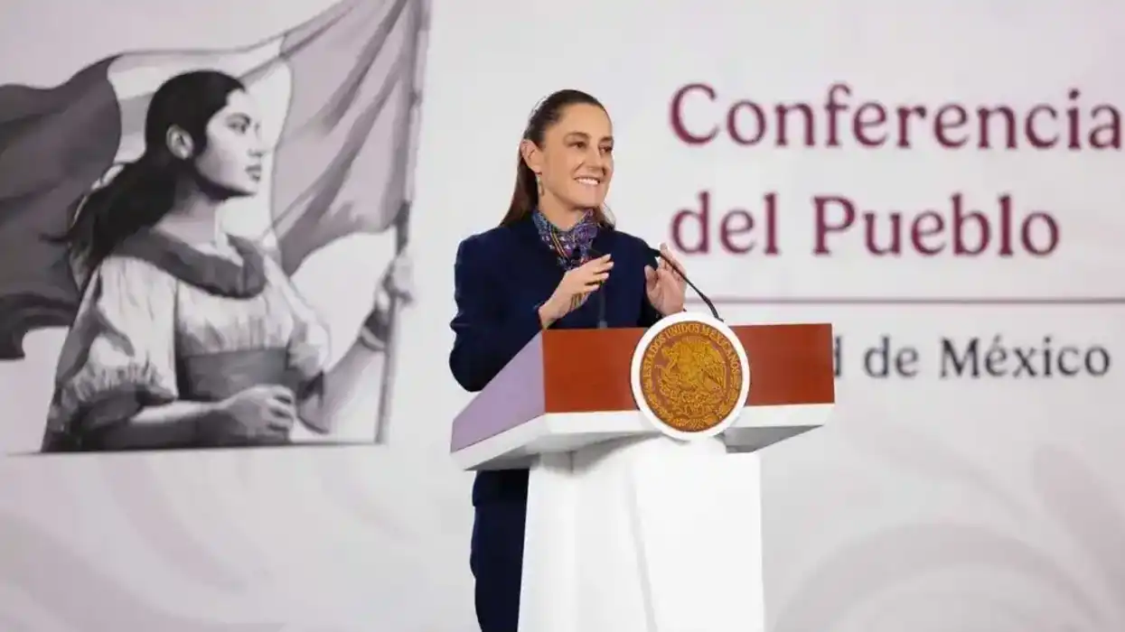 Speaker at a podium during "Conferencia del Pueblo," with large mural in the background.