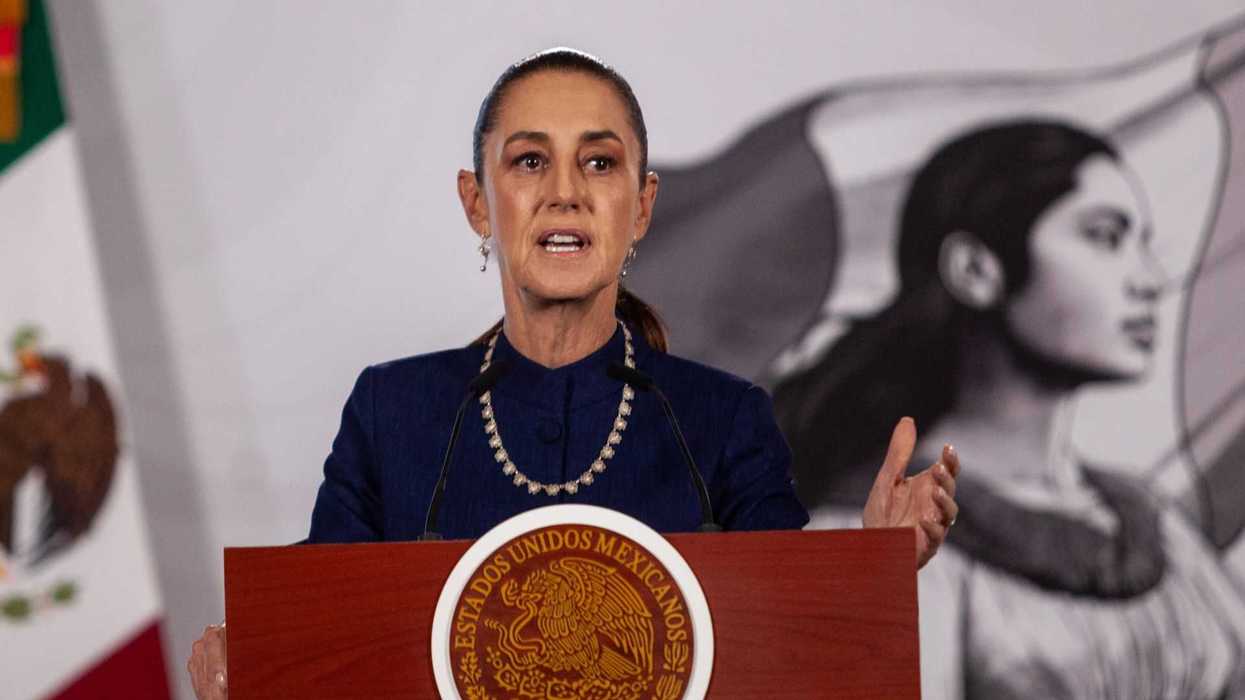 Speaker at podium with Mexican emblem, mural background.