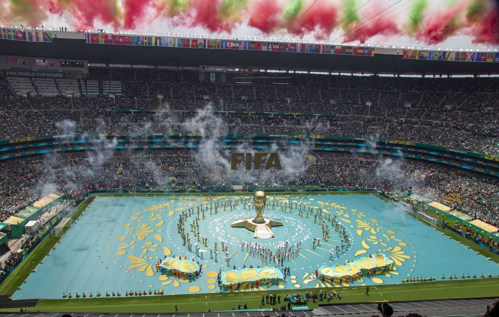Stadium crowd, FIFA World Cup opening ceremony with colorful smoke and trophy display.