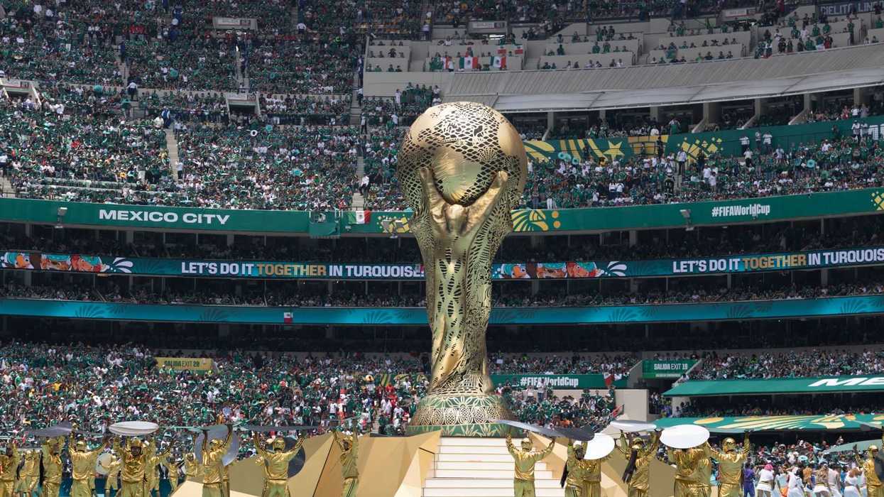 Stadium event with giant trophy replica surrounded by performers and large crowd.