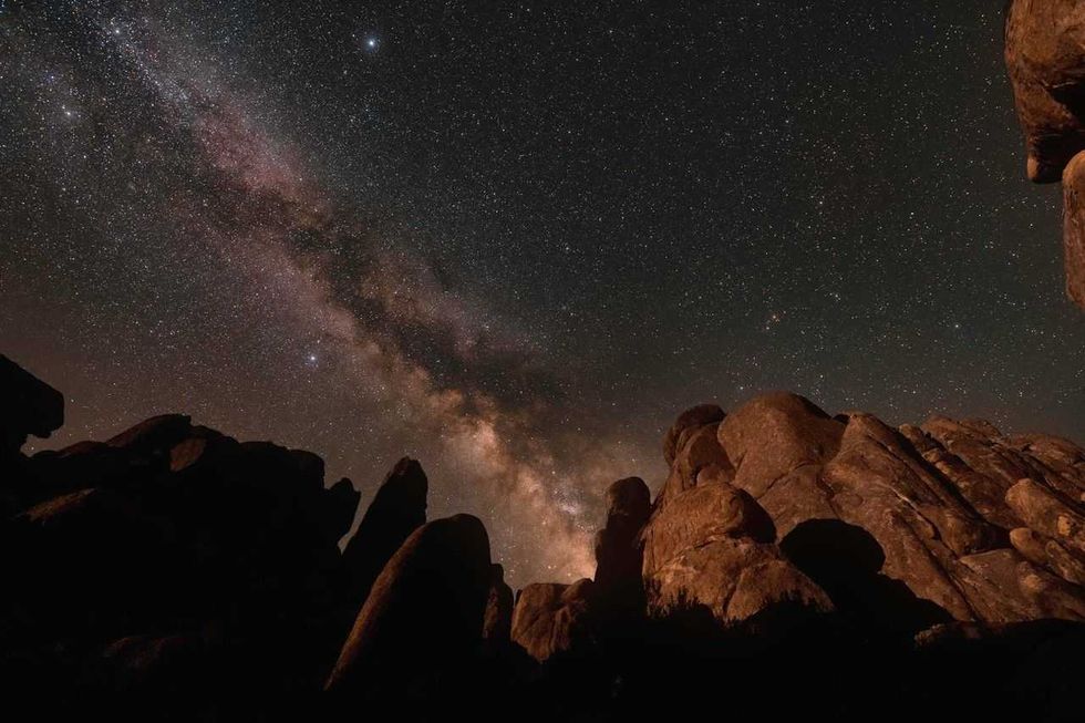 Starry sky with the Milky Way over silhouetted rocky terrain at night.