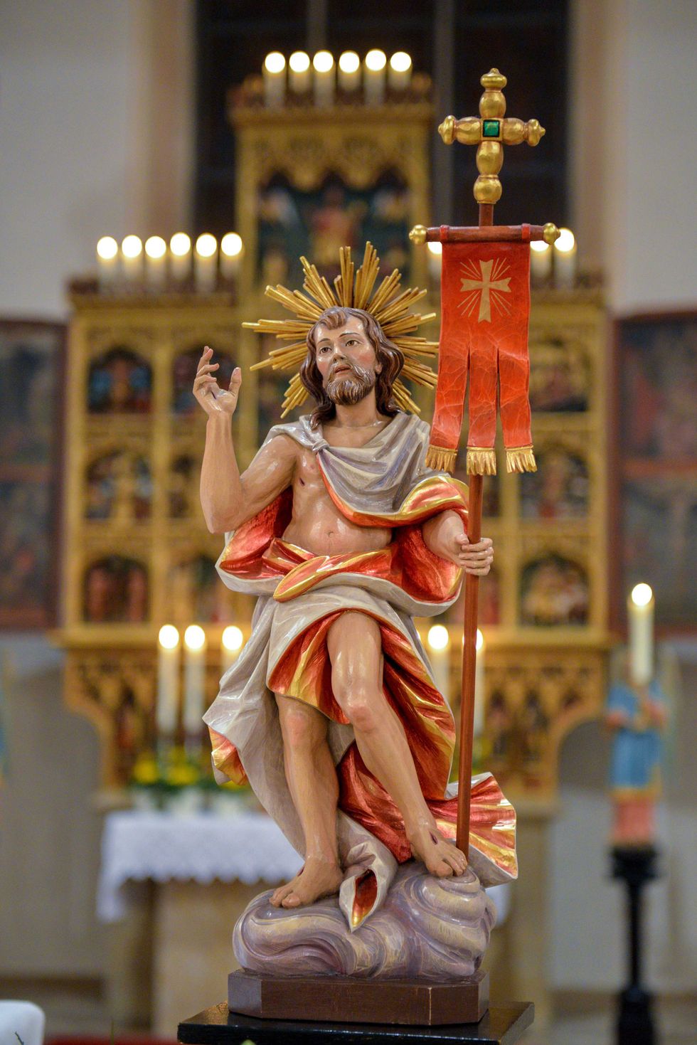 Statue of Jesus with a halo and banner in a candle-lit church setting.