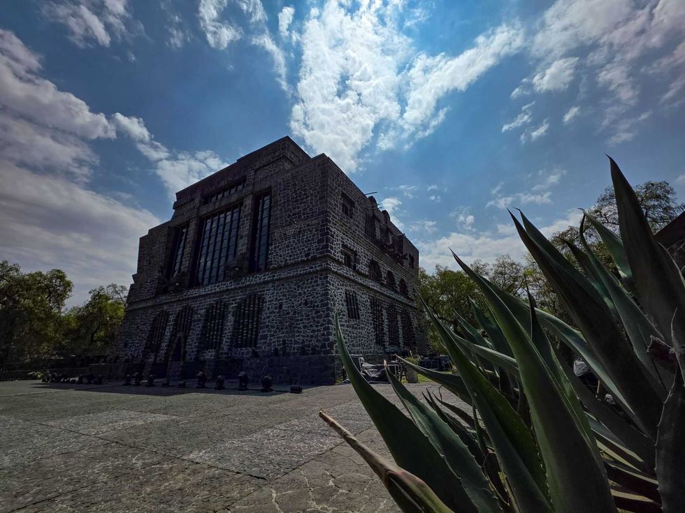 Stone building under a cloudy sky with agave plants in the foreground.