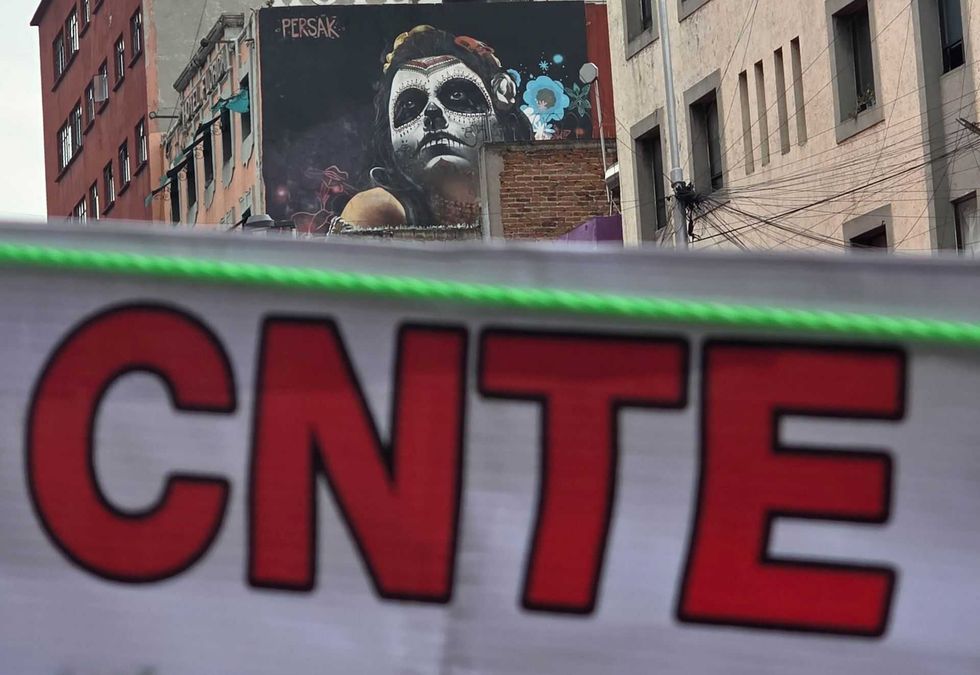 Street art of a face with skull makeup behind a "CNTE" banner in an urban setting.