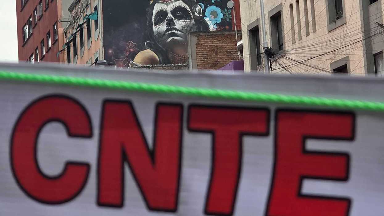 Street art with a skull face, "CNTE" banner in foreground, urban buildings in background.