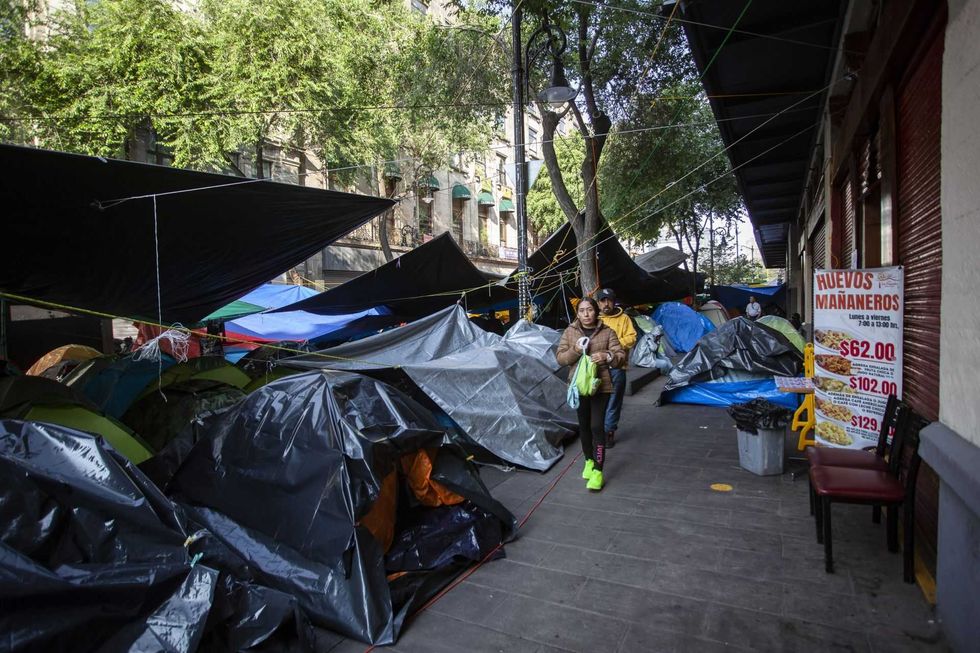 Street lined with tarps and tents; people walking; sign with breakfast prices.