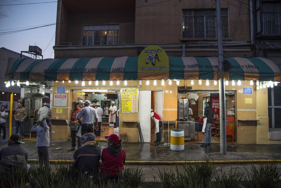 Street taco stand at dusk with people gathered under bright lights.