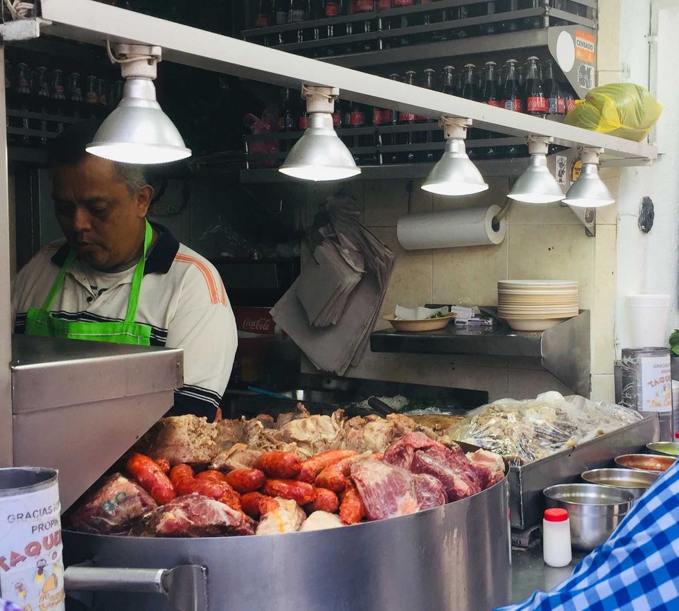 Street vendor with assorted meats under lights at a bustling food stall.