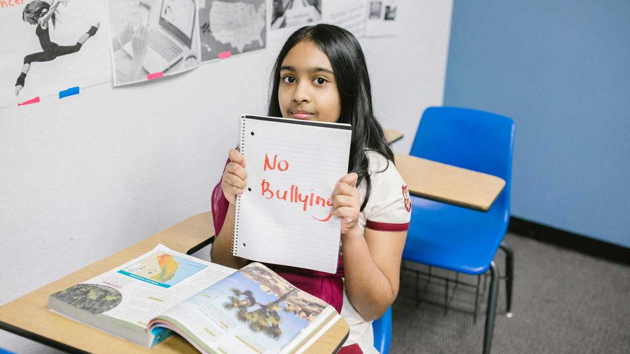 Student holding a "No Bullying" sign in a classroom setting.
