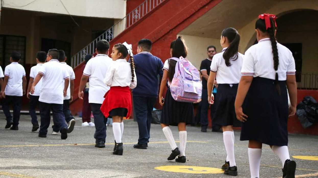 Students in uniform walking towards a school building in groups.