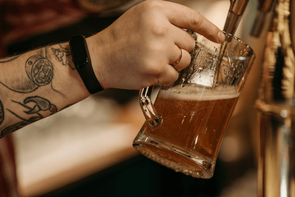 Tattoed hand pouring beer into a glass mug from a tap.