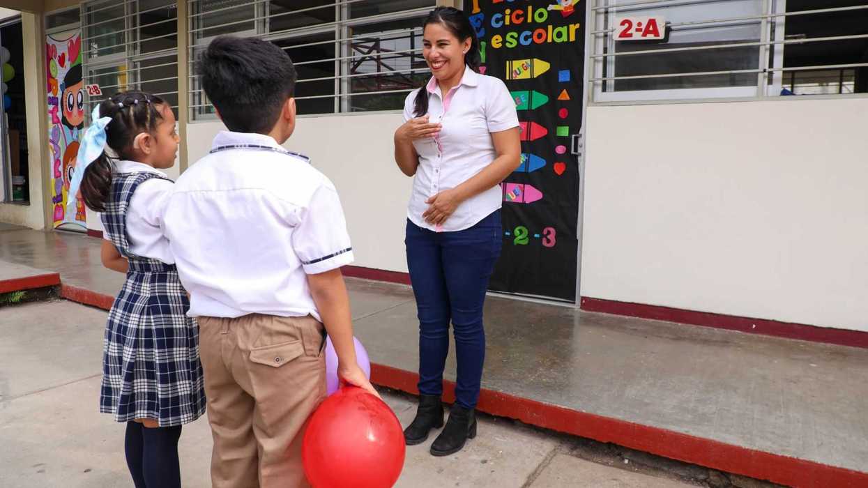 Teacher greeting two students with a balloon outside a decorated classroom door.