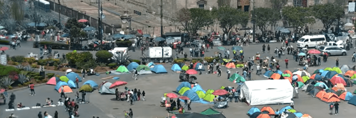 Tents and people gathered in a city square near a large historic building.
