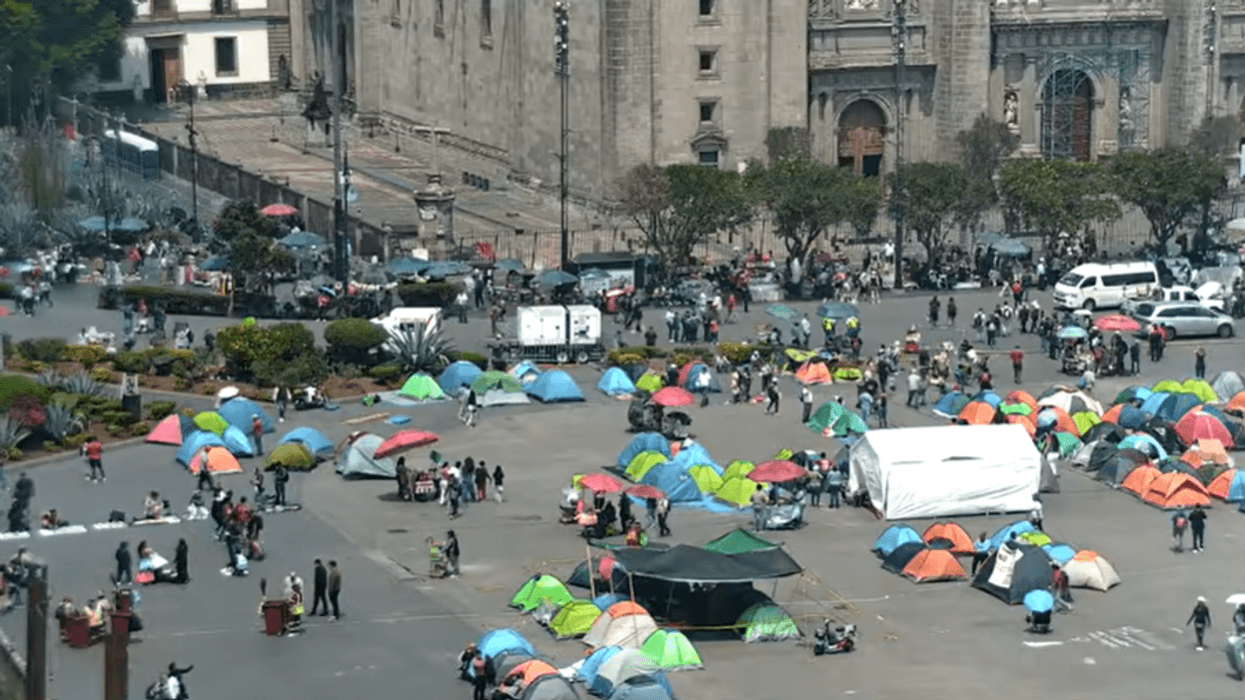 Tents and people gathered in a city square near a large historic building.