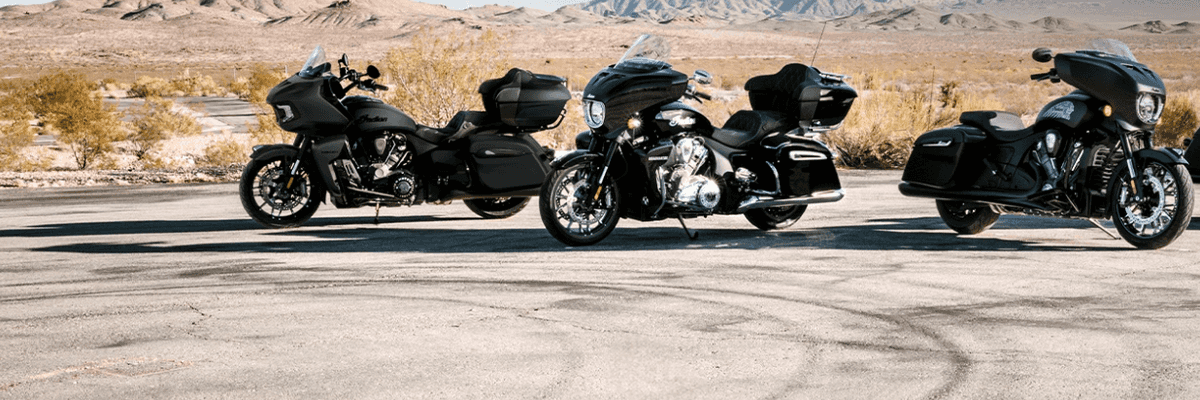 Three black motorcycles parked on desert road with mountains in background.