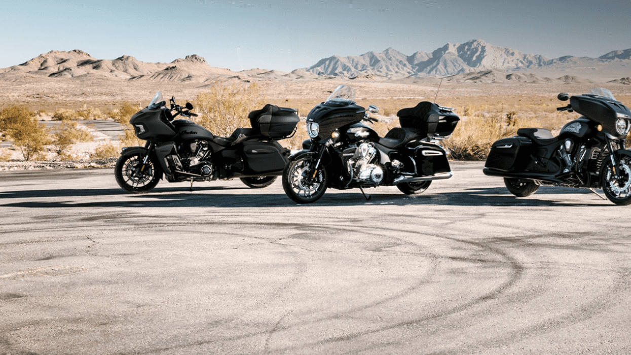 Three black motorcycles parked on desert road with mountains in background.