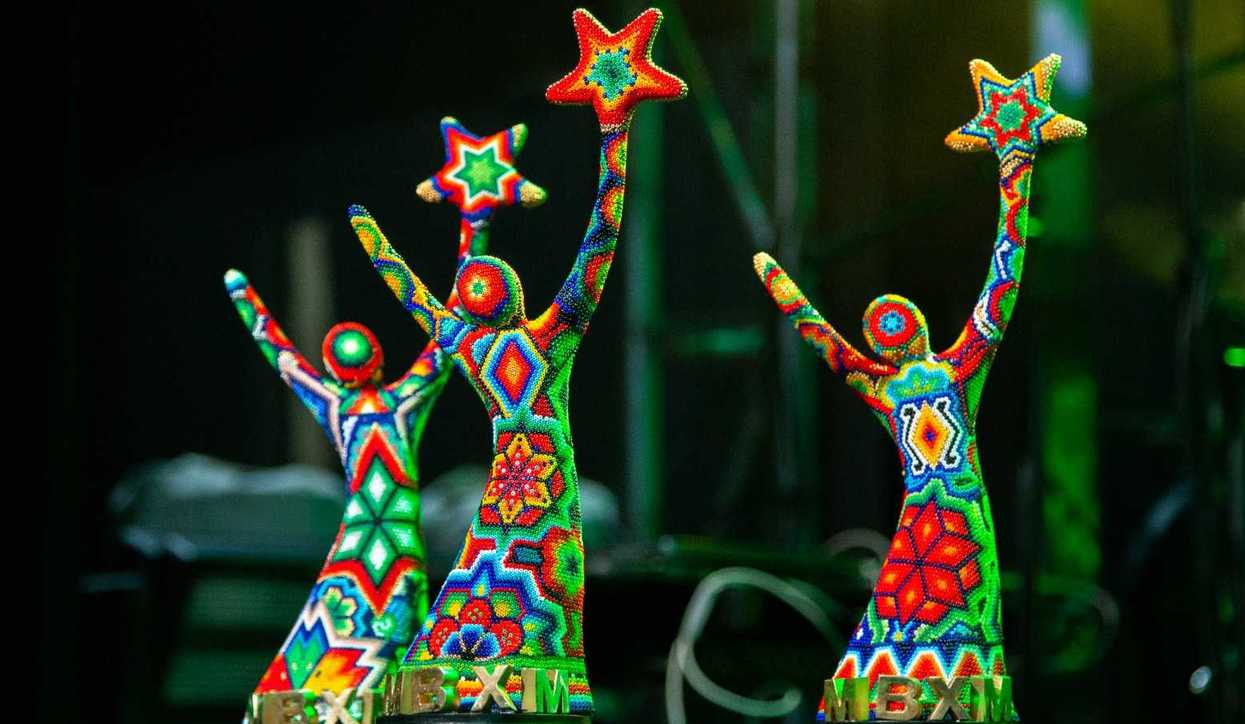 Three colorful, beaded sculptures holding stars, displayed in a dimly lit environment.