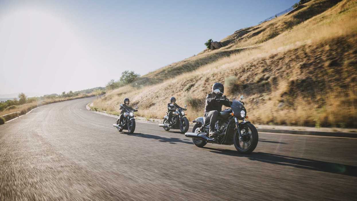Three motorcyclists riding on a scenic road near sunlit hills.