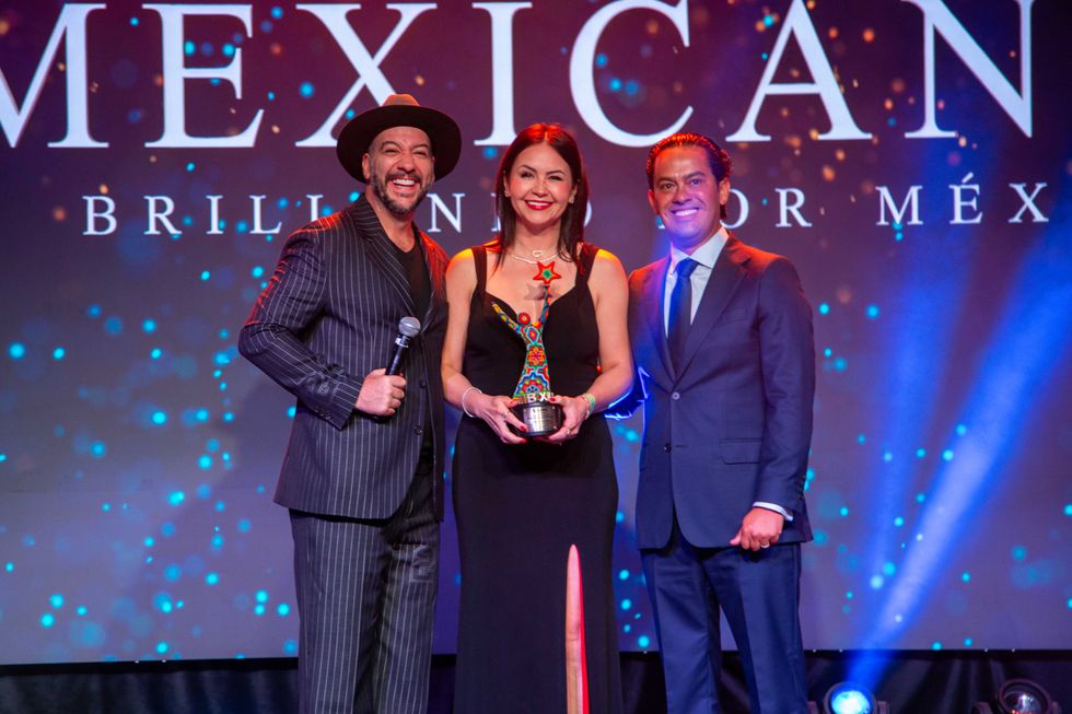 Three people posing on stage with an award, under colorful lighting.